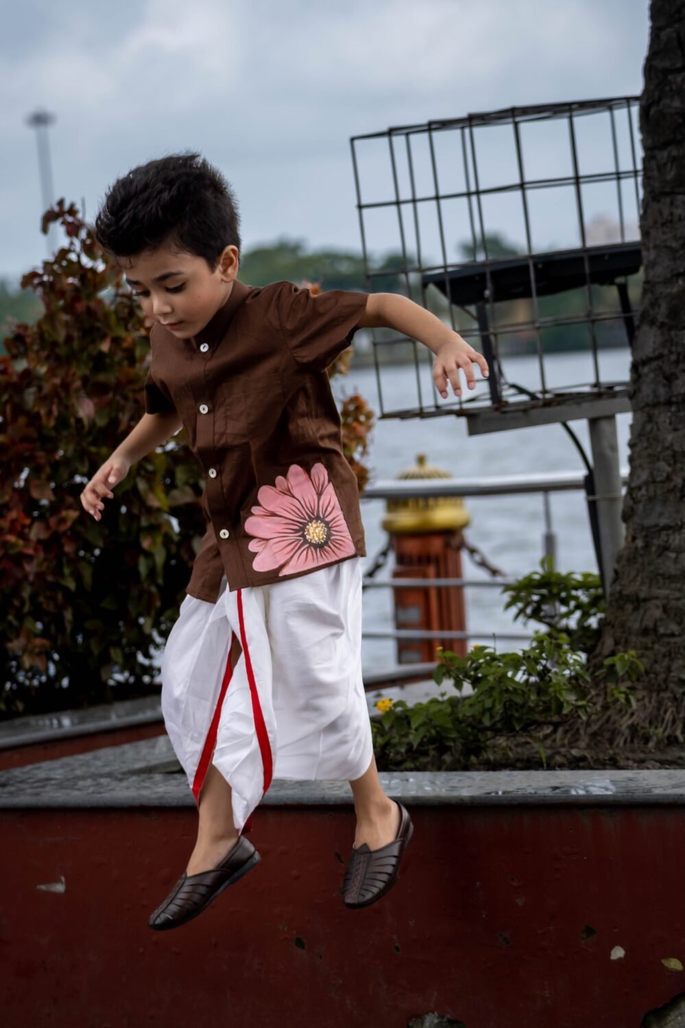 Young boy running happily outdoors in Kisholoy chocolate brown hand-painted shirt
