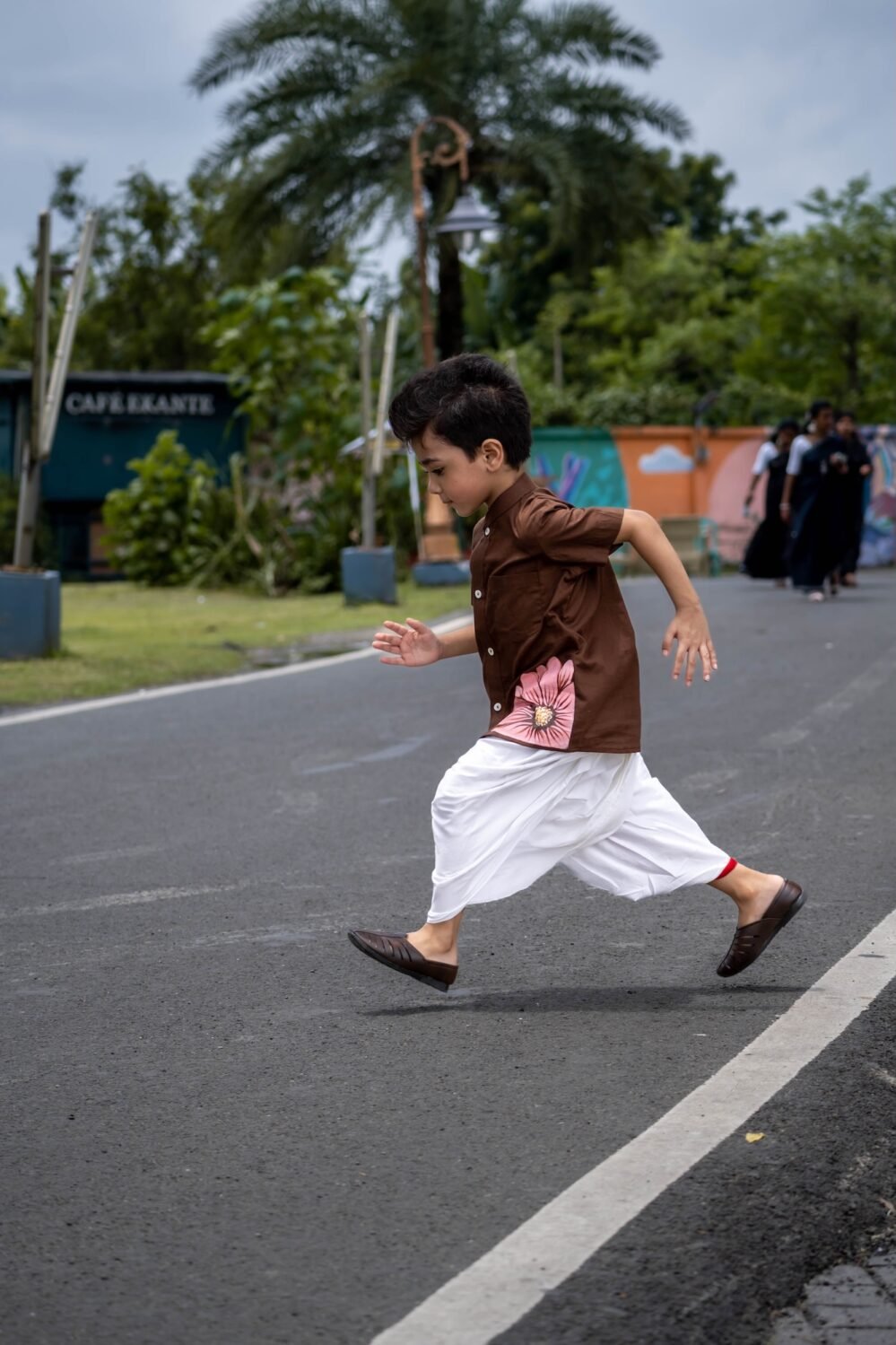 Boy running outdoors wearing Kisholoy chocolate brown hand-painted shirt and white dhoti