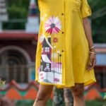 Close-up of hand-painted house and pink flower artwork on yellow hand woven cotton shirt.
