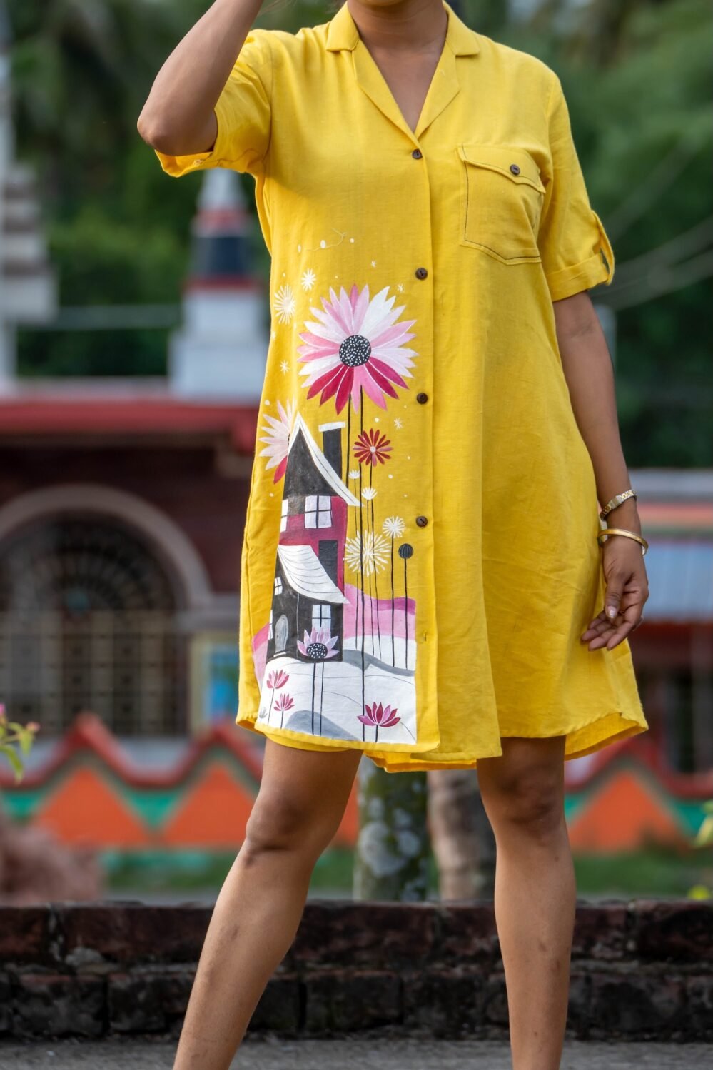 Close-up of hand-painted house and pink flower artwork on yellow hand woven cotton shirt.