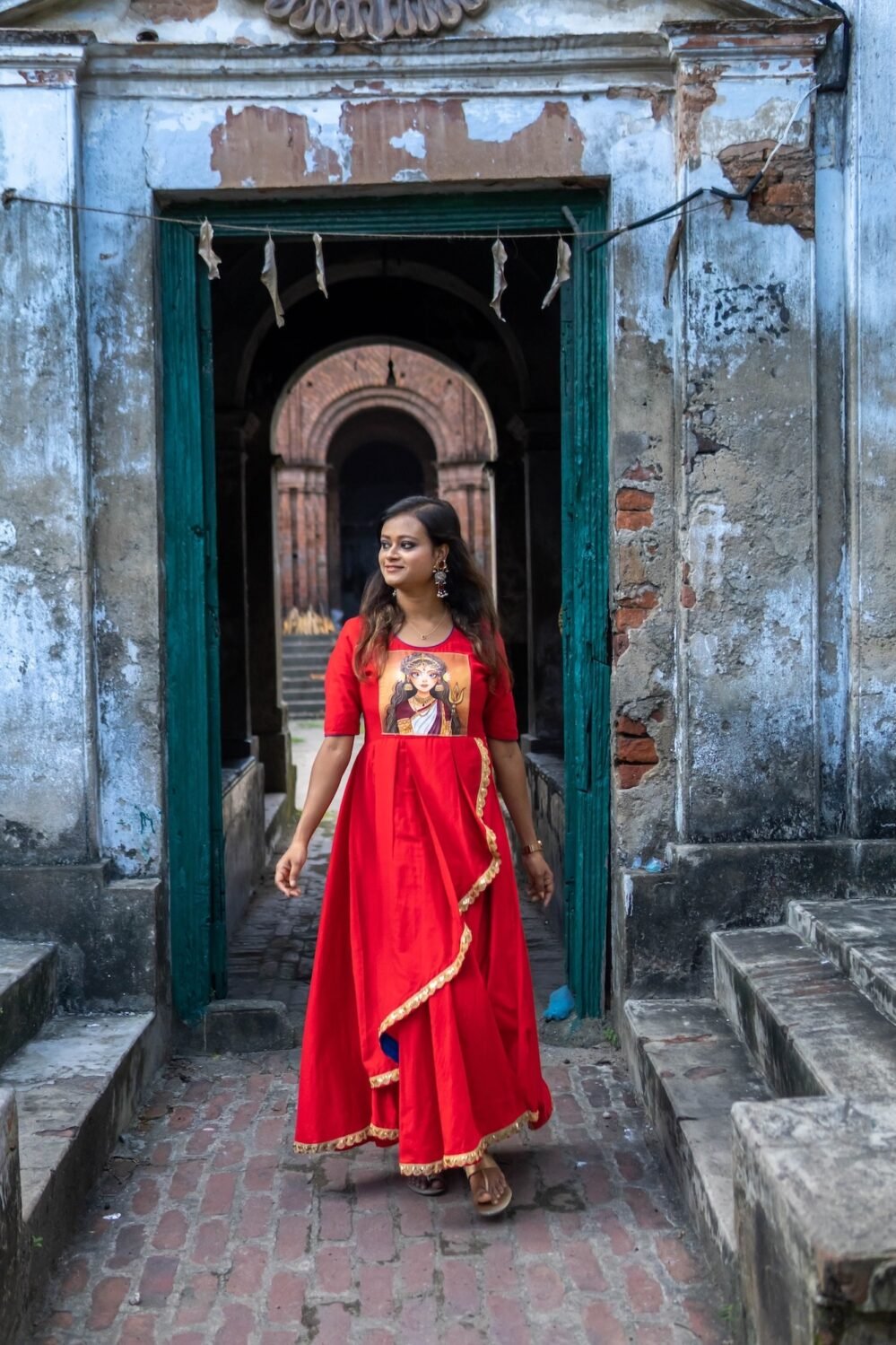 Model walking through a historical doorway wearing the red hand-painted Maa Durga gown.