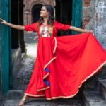 Model spreading the wide skirt flare of the hand-painted red Maa Durga gown in a doorway.