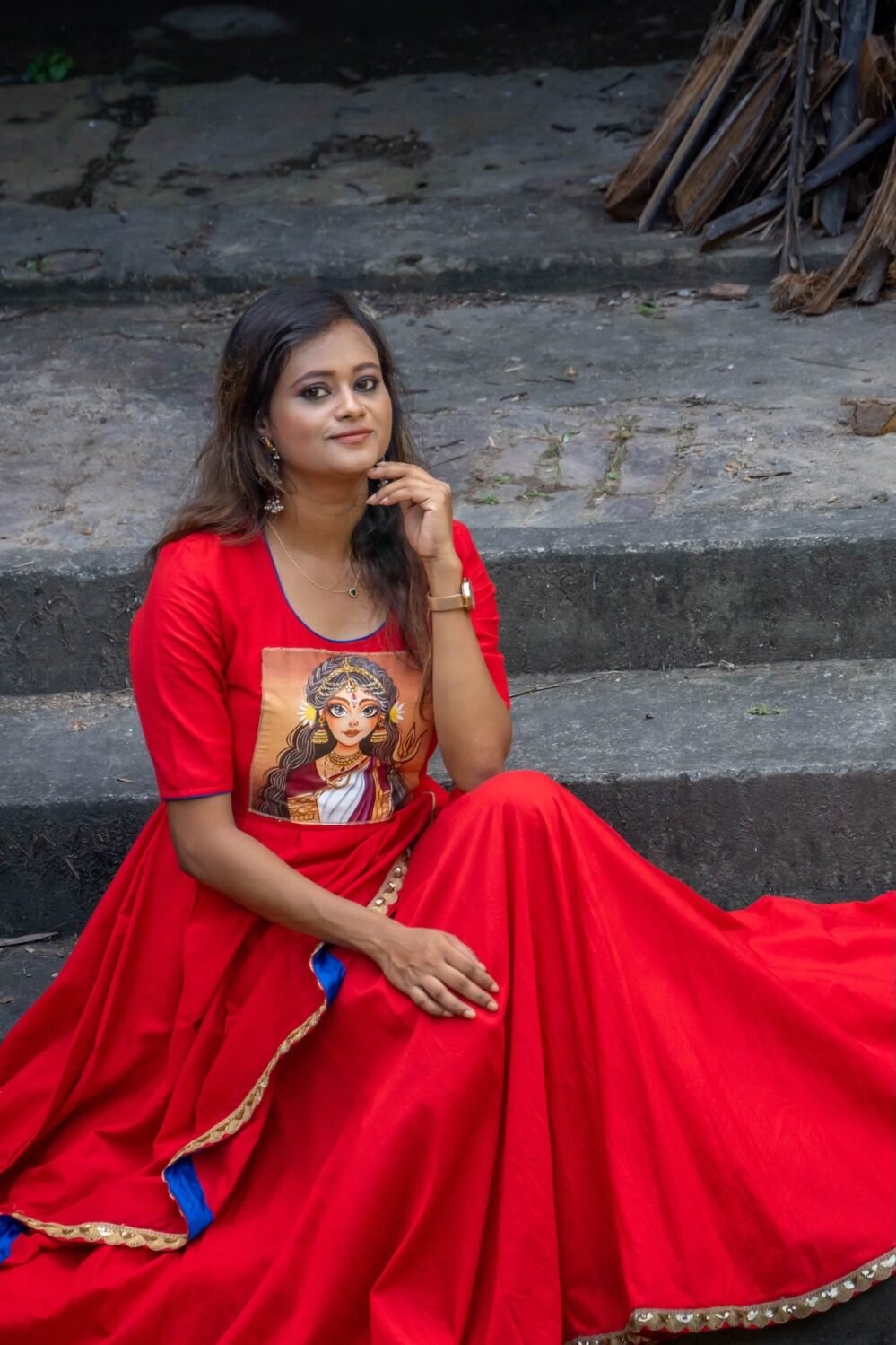 Mid-shot of model seated wearing red malai cotton gown with hand-painted Maa Durga chest artwork.