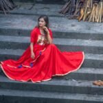 Model seated on heritage stone steps wearing the red hand-painted Maa Durga Trinayana Crimson Gown.