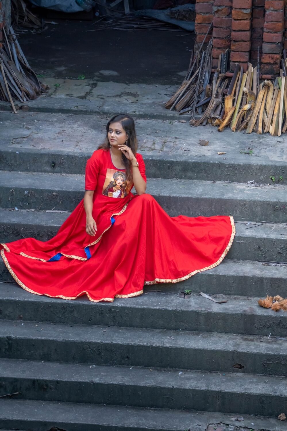 Model seated on heritage stone steps wearing the red hand-painted Maa Durga Trinayana Crimson Gown.