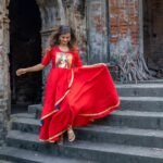 Model stepping down historic stone stairs wearing the flared hand-painted red Durga gown.