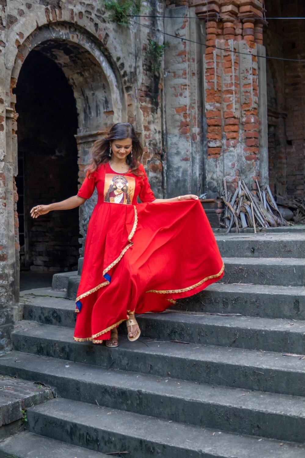 Model stepping down historic stone stairs wearing the flared hand-painted red Durga gown.