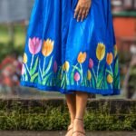 Close-up detail of hand-painted pink, orange, and yellow tulips on the hem of a royal blue dress.