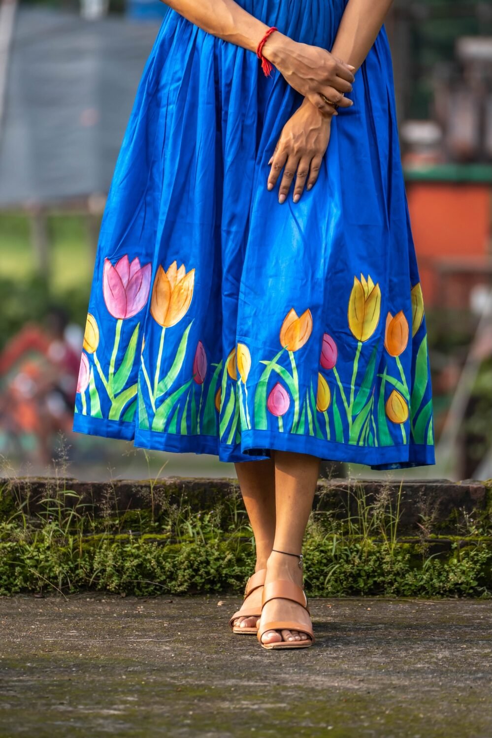 Close-up detail of hand-painted pink, orange, and yellow tulips on the hem of a royal blue dress.